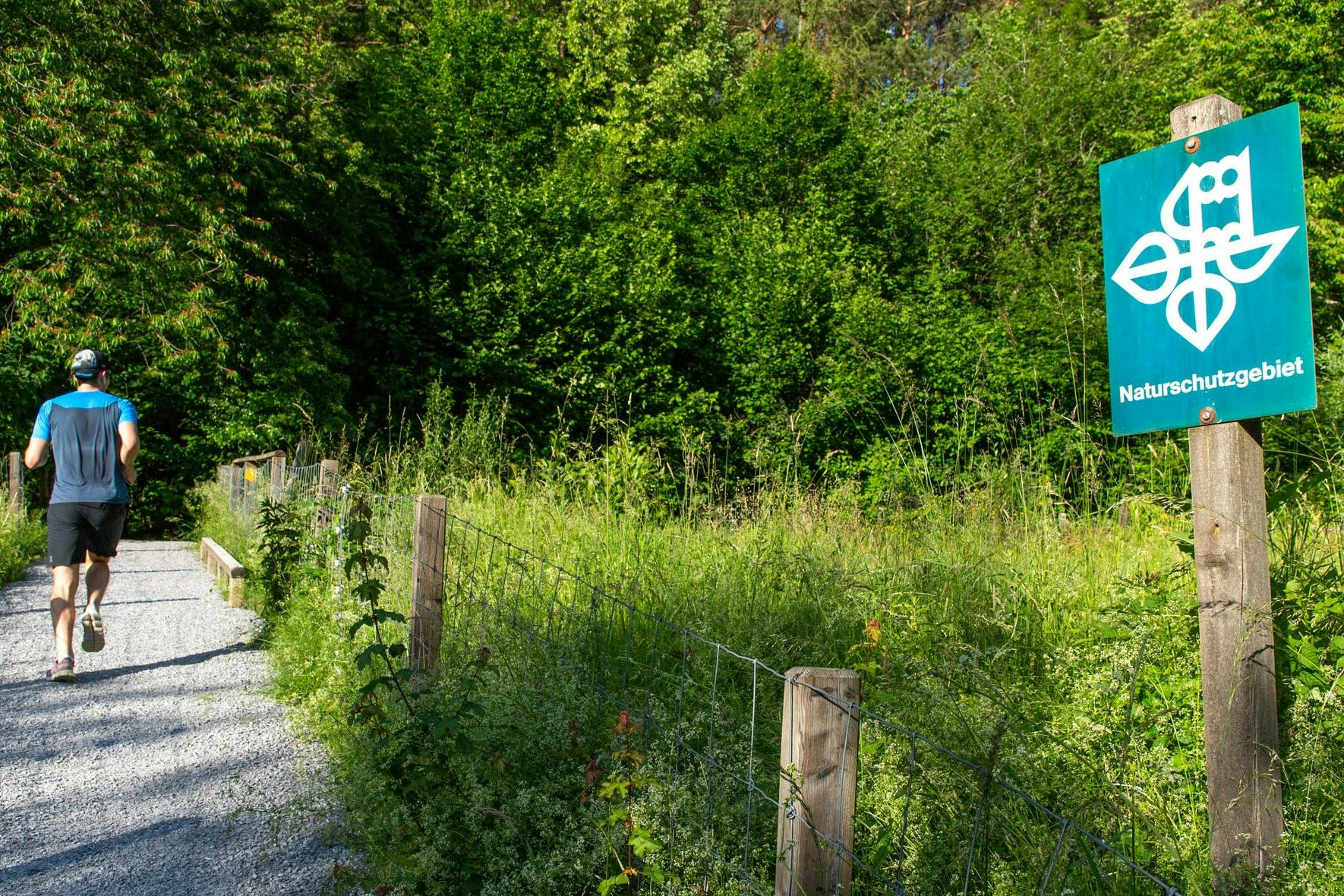 Ein Jogger rennt auf einem Kiesweg an einem Schild eines Naturschutzgebiets vorbei.
