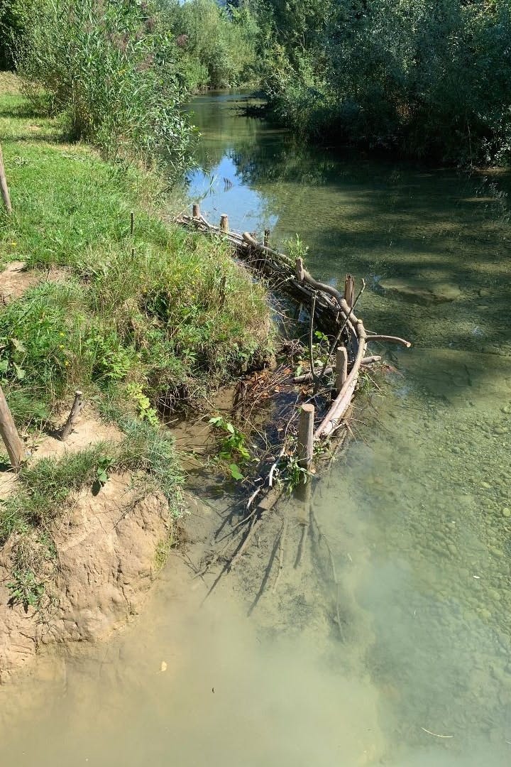 Ein Bach mit aus Holzpflöcken und Ästen erstelltem Flechtzaun zur Uferbefestigung.