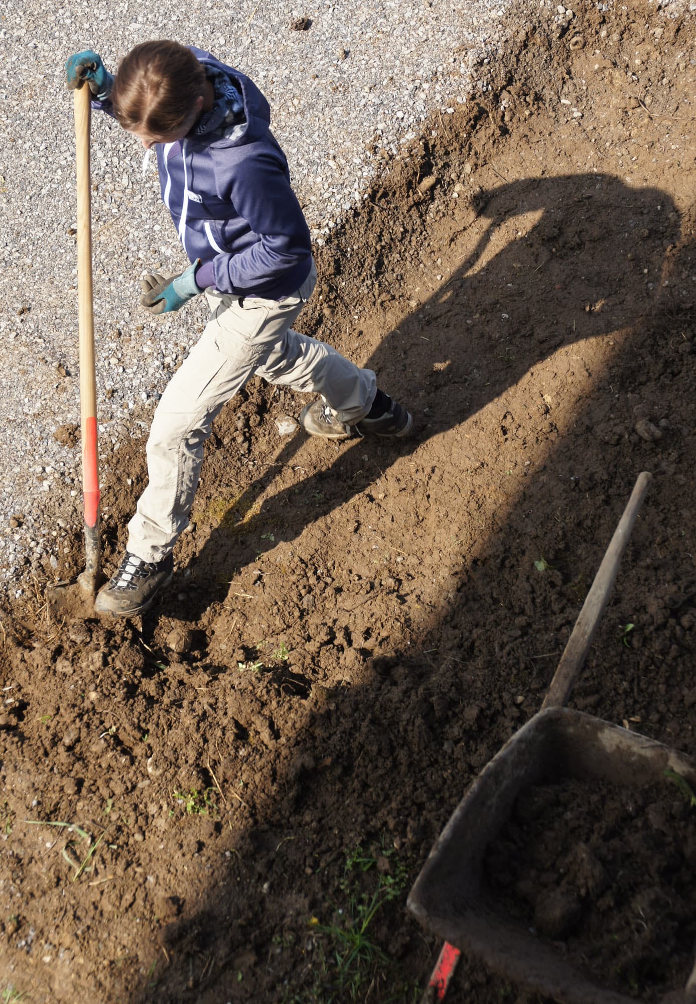 Ein Kind schaufelt mit einer Schaufel Erde in eine Schubkarre.