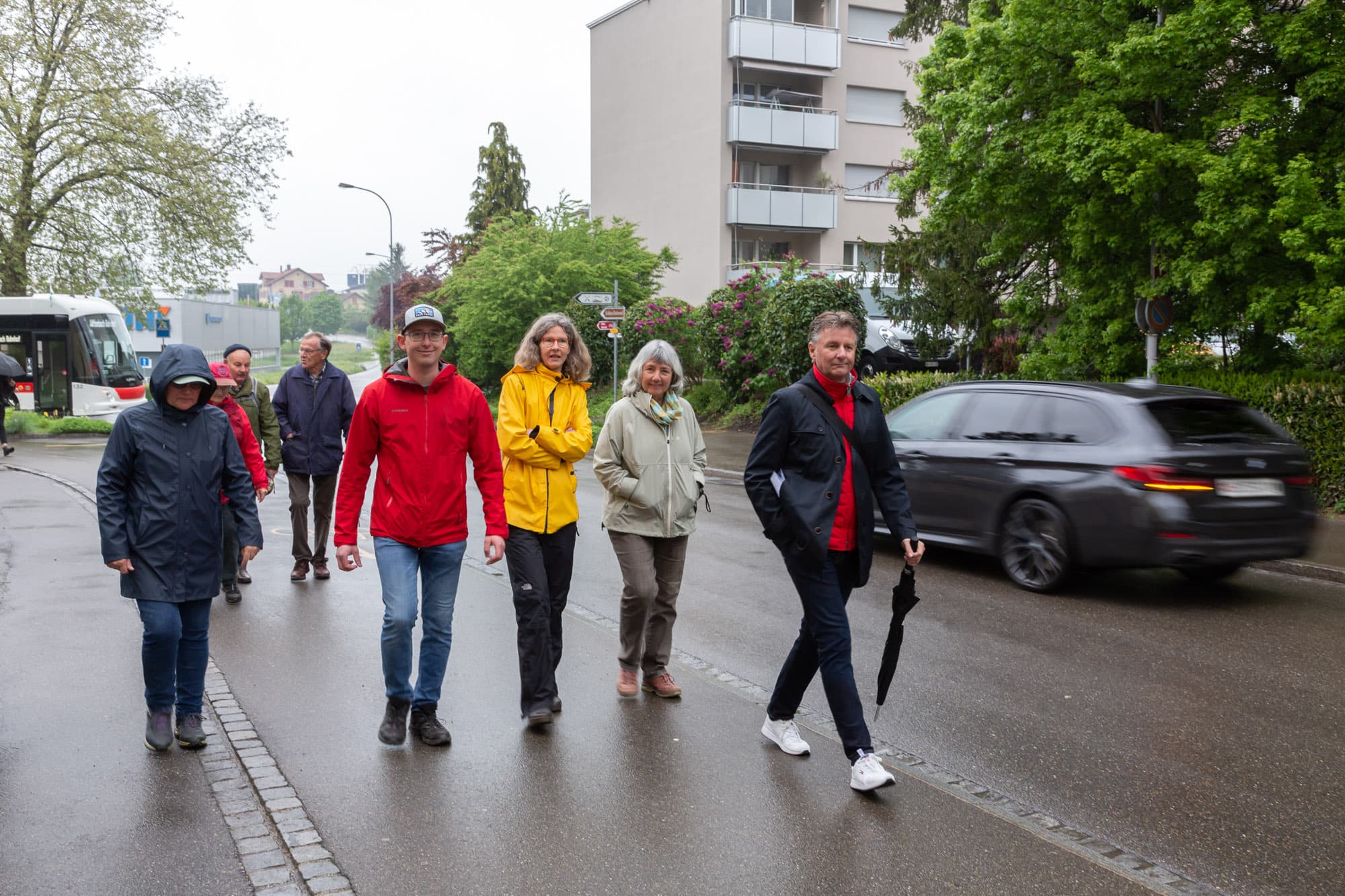 Gruppe von Erwachsenen spaziert auf dem Trottoir durch ein Quartier.