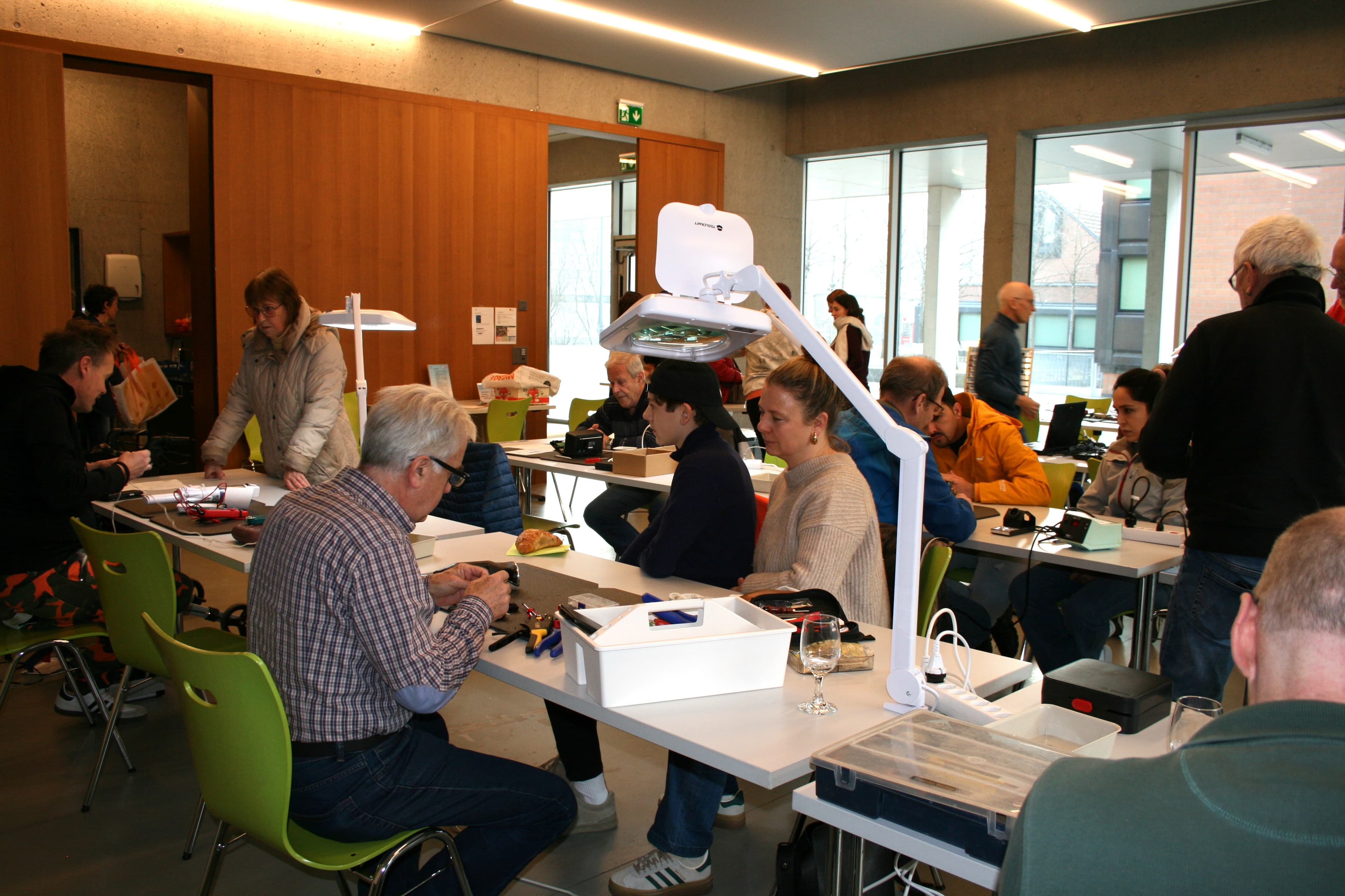 Menschen sitzen an mehreren Tischen und reparieren Gegenstände.