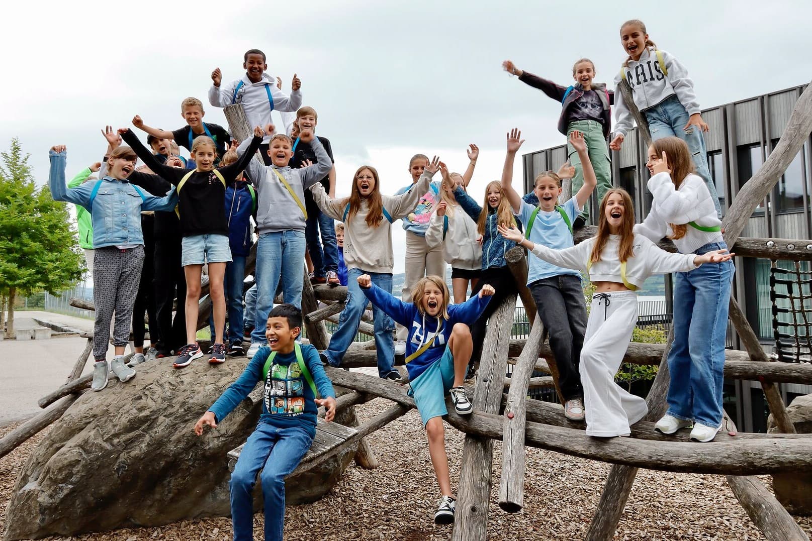 Jubelnde Kinder stehen mit den Händen in der Luft auf einem Klettergerüst und einem grossen Stein auf dem Spielplatz