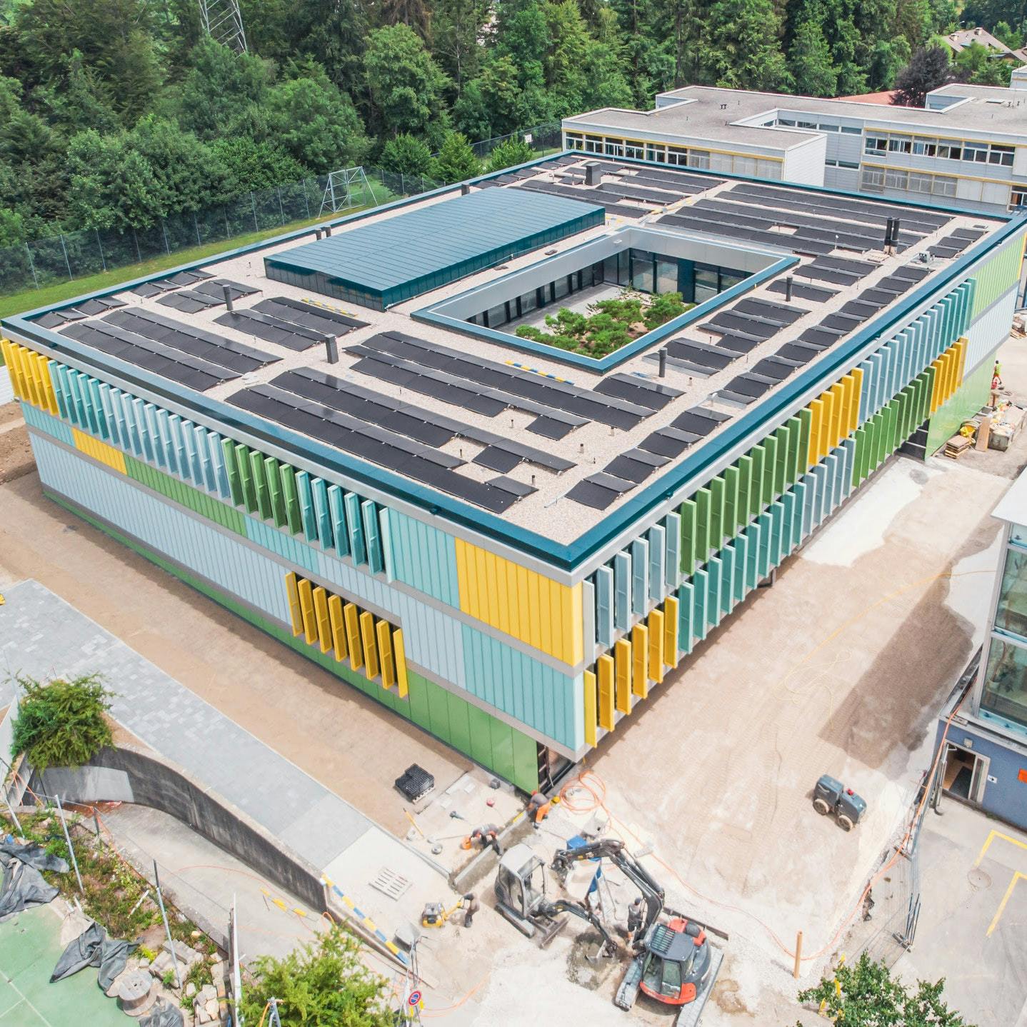 Luftaufnahme von einem modernen rechteckigen Schulgebäude mit Photovoltaik-Anlage auf dem Dach