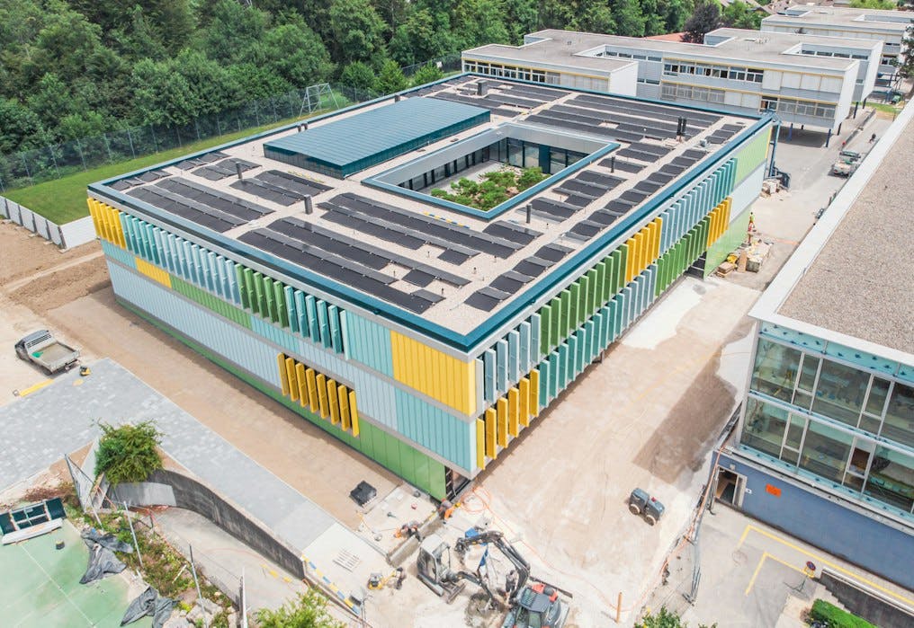 Luftaufnahme von einem modernen rechteckigen Schulgebäude mit Photovoltaik-Anlage auf dem Dach