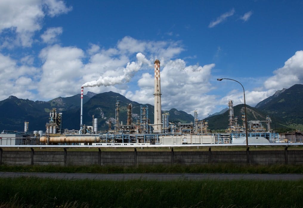 Erdölraffinerie mit mehreren Kaminen und einem Bergpanorama im Hintergrund.