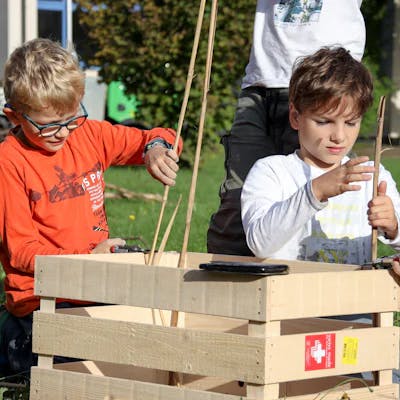 Zwei Jungs bauen etwas mit Holzstäben und einer Holzkiste.