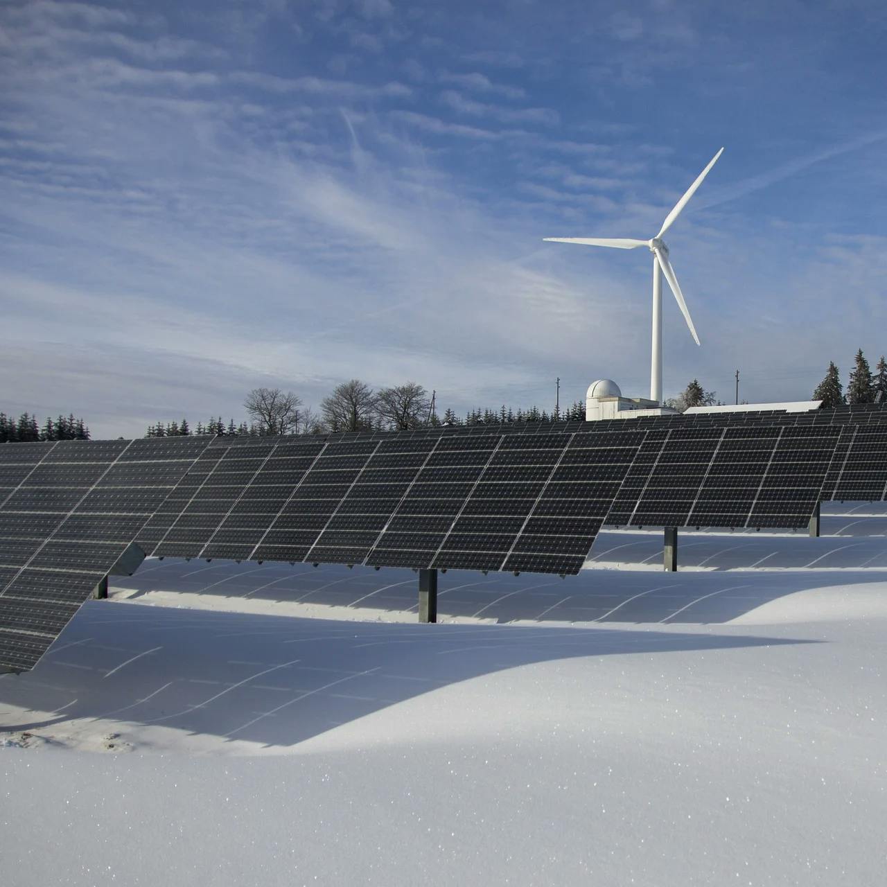 Photovoltaik-Anlage im Schnee, dahinter steht ein Windrad.