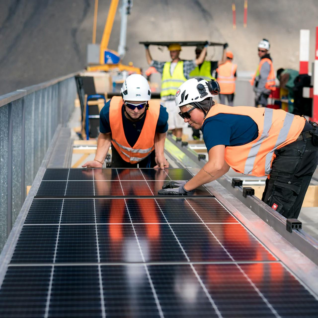 Arbeiter installieren Solarpanels auf einer Staumauer.