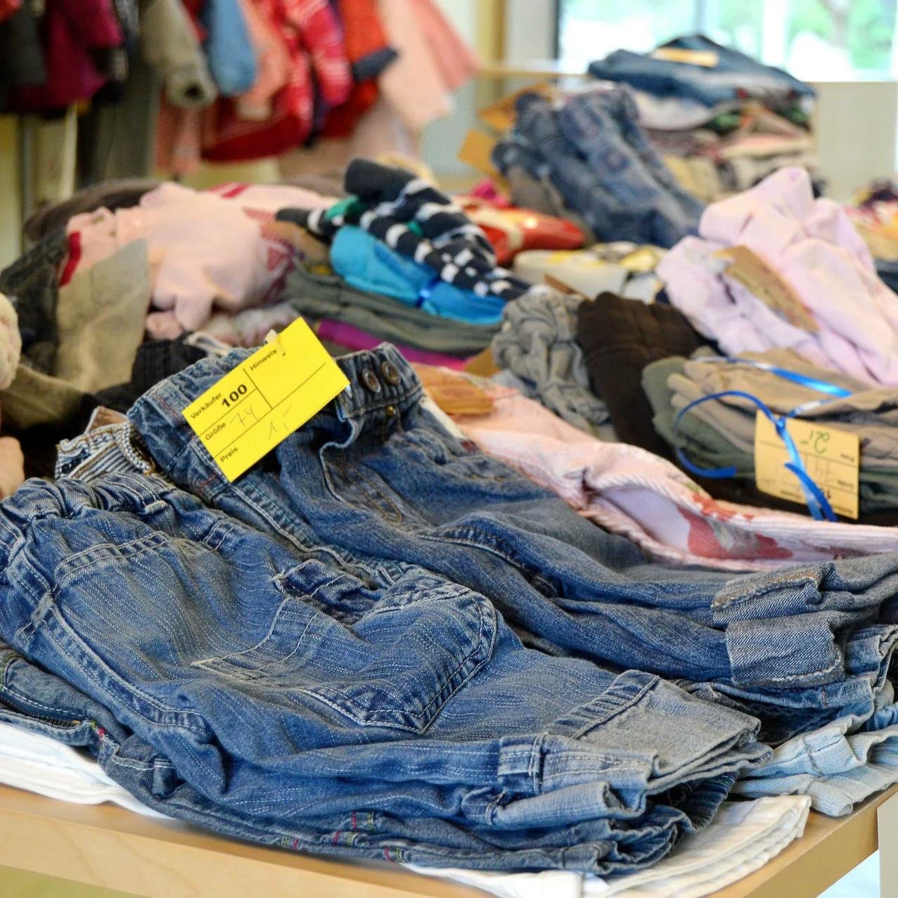 Jeans und andere Kleider liegen auf einem Tisch in einem Secondhand-Laden.