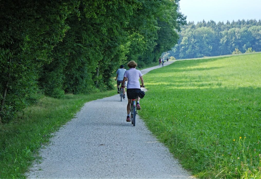 Weg neben einem Wald, auf dem Menschen mit dem Fahrrad davonfahren.