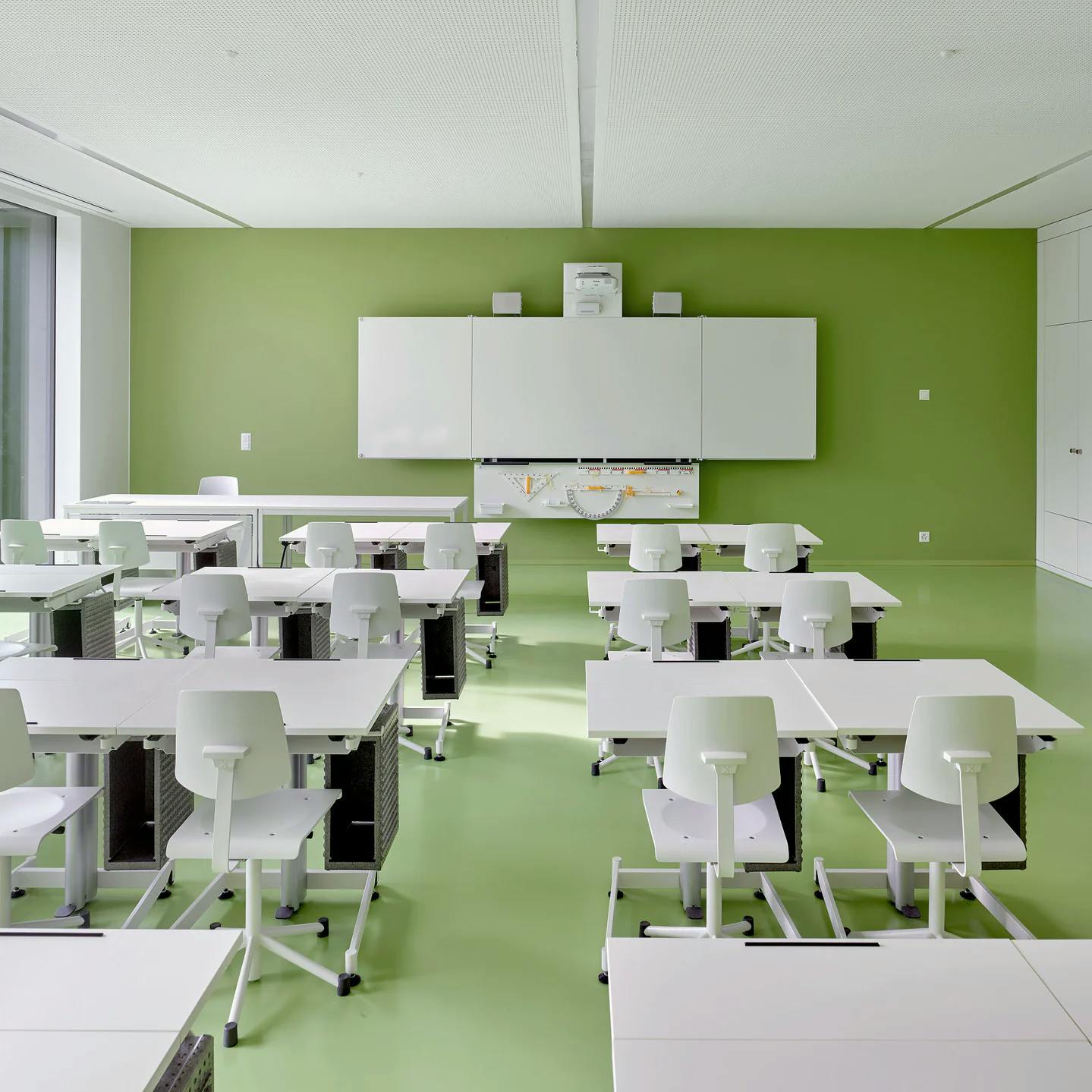 Modernes Klassenzimmer: Ein Schulzimmer mit grüner Wand und Boden und weissen Möbeln im umgebauten Vignettaz-Schulhauses in Freiburg.
