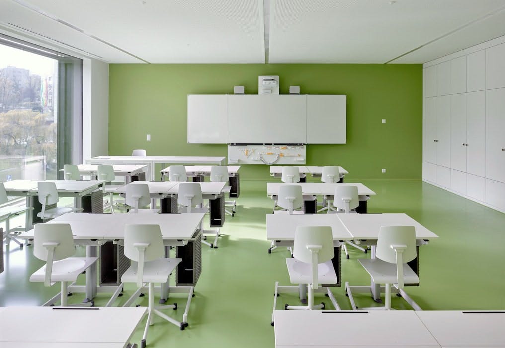 Modernes Klassenzimmer: Ein Schulzimmer mit grüner Wand und Boden und weissen Möbeln im umgebauten Vignettaz-Schulhauses in Freiburg.